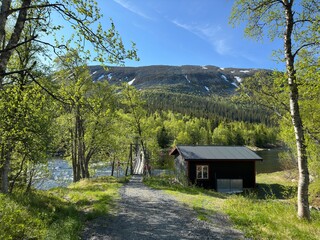 Cabin nestled near a river with a suspension bridge and a mountain backdrop in north Sweden.
