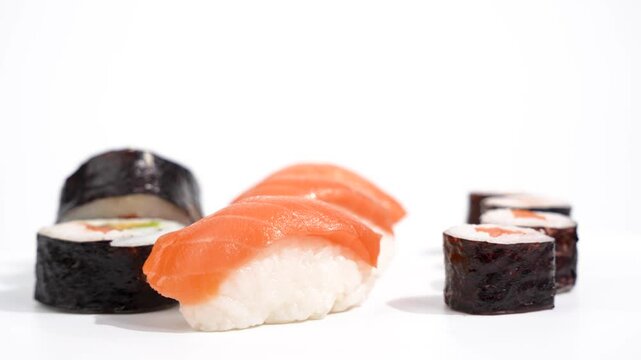 Sushi casually arranged rotating on white background. Various sushi, rolls and nigiri casually arranged on a white table. The arrangement looks natural and attractive.