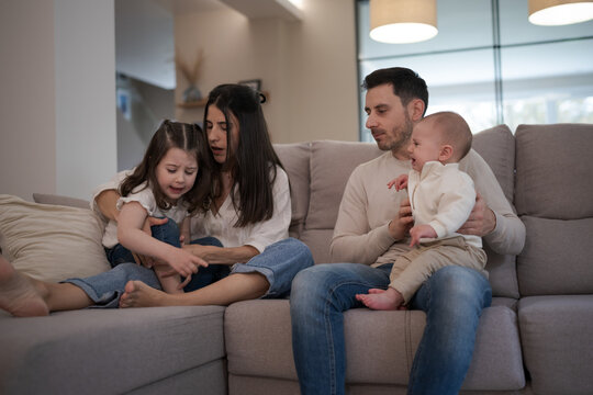 Parents comforting crying children on sofa in living room - Powered by Adobe