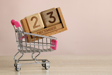 Shopping cart carrying wooden calendar showing december 23rd for christmas shopping concept
