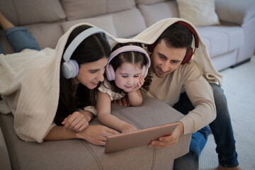 Family enjoying digital tablet under blanket, wearing headphones