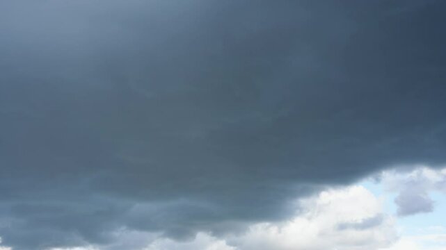Timelapse of Dark Thunderclouds. Thick dark clouds cover the sky, foreshadowing an approaching thunderstorm. The mood seems dramatic and tense.