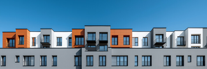 A row of apartment buildings with balconies and windows. The buildings are mostly white and brown. The sky is blue and clear