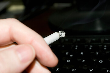 Close-up of hand holding cigarette over a computer keyboard