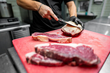 A chef slices raw beef on a red cutting board in a professional kitchen, showcasing precision and culinary skill. The fresh marbled texture of the meat highlights quality and craftsmanship