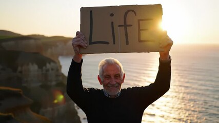 Senior man celebrates life on cliff at sunset with cardboard sign - Powered by Adobe