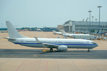 White airplane taxiing at the airport, on the steering track, surrounded by airport parking lots and buildings