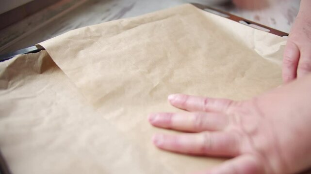 Hands smoothing parchment paper on baking tray