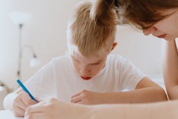 A loving mother and her son work together on homework at the kitchen table, symbolizing family...