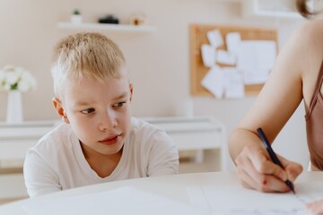 Naklejka premium A loving mother and her son work together on homework at the kitchen table, symbolizing family support, education, and care. The scene highlights the importance of parental guidance