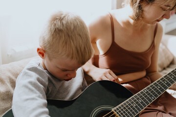 Mother and son playing guitar together, family love. The child wears a hearing aid, highlighting...