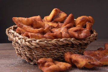 Traditional Crostoli Pastries in a Wicker Basket on Rustic Wooden Table, talian treats are sprinkled with sugar and arranged in an inviting, homemade style. Brazilian food.