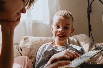 Mother and son playing guitar together, family love. The child wears a hearing aid, highlighting...