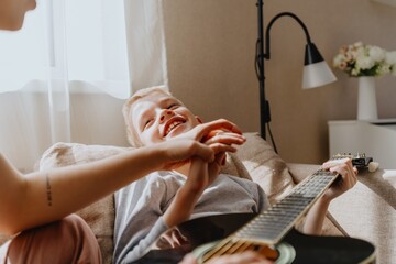 Obraz premium Mother and son playing guitar together, family love. The child wears a hearing aid, highlighting inclusivity and the universal language of music. Authentic, unedited photo captures emotions