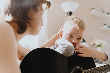 Mother and son playing guitar together, family love. The child wears a hearing aid, highlighting...