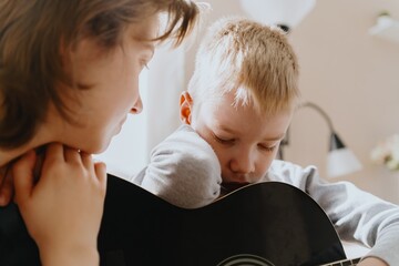 Mother and son playing guitar together, family love. The child wears a hearing aid, highlighting...