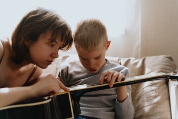 Mother and son playing guitar together, family love. The child wears a hearing aid, highlighting...