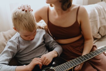 Mother and son playing guitar together, family love. The child wears a hearing aid, highlighting...