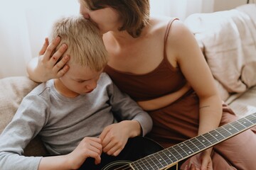 Mother and son playing guitar together, family love. The child wears a hearing aid, highlighting...