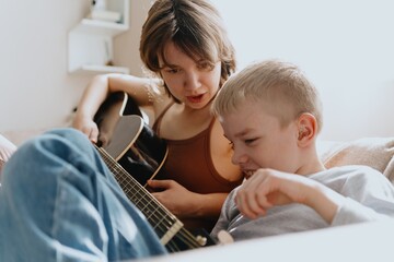 Mother and son playing guitar together, family love. The child wears a hearing aid, highlighting...