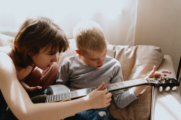 Mother and son playing guitar together, family love. The child wears a hearing aid, highlighting...
