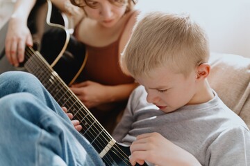 Mother and son playing guitar together, family love. The child wears a hearing aid, highlighting...