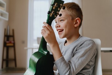 Mother and son playing guitar together, family love. The child wears a hearing aid, highlighting...