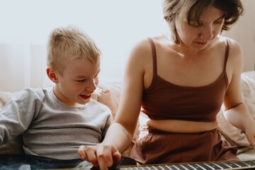 Mother and son playing guitar together, family love. The child wears a hearing aid, highlighting...