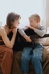 Mother and son playing guitar together, family love. The child wears a hearing aid, highlighting inclusivity and the universal language of music. Authentic, unedited photo captures emotions