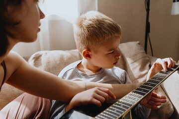 Mother and son playing guitar together, family love. The child wears a hearing aid, highlighting...