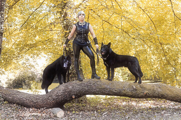 Eine schwarzgekleidete Frau mit zwei schwarzen Hunden auf einem Baumstamm