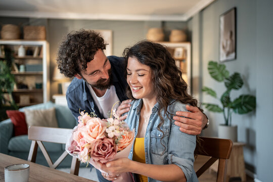Man giving flowers to woman at home: romantic surprise