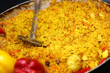 Plov cooked in a cauldron. Food at the food court. Plov with meat, onions, carrots and spices. Tasty and hot food. Fair. Tasty plov in a burning cauldron in the open air. Street food festival
