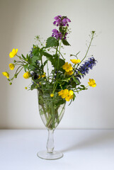 Wildflower Bouquet in Ornamental Vase. A vibrant bouquet of wildflowers featuring yellow buttercups, purple bugleweed (Ajuga), and other field blooms arranged in an ornate ceramic vase.