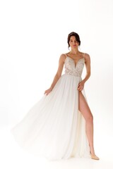 Elegant model poses in flowing white dress with intricate details and high slit against bright background