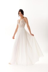 Elegant woman in flowing white dress poses gracefully against a plain background showcasing bridal...