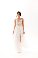 Model walks gracefully in a flowing white dress showcasing elegance and beauty in a softly lit studio setting