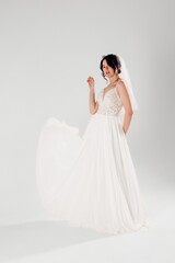 Naklejka premium Bride in elegant white dress with flowing fabric poses gracefully in studio setting during daytime