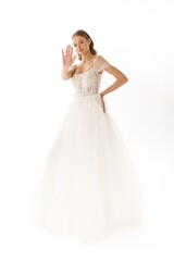 Elegant bride in a wedding dress poses against a white background while playfully waving her hand to the camera