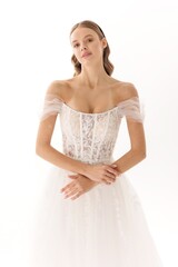 Elegant bride wearing a lace wedding gown with off-shoulder sleeves and a soft hairstyle in a light studio setting