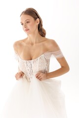 Fototapeta premium Elegant bride in a delicate wedding gown adjusting her dress in a bright studio setting