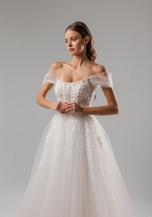 Fototapeta premium Elegant bride in white dress poses gracefully against a neutral background during a modern fashion shoot