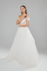 Fototapeta premium Elegant bride posing in a romantic off-shoulder wedding gown with tulle skirt against a neutral background