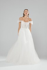 Elegant bride wearing a white off-the-shoulder wedding gown in a minimalist studio setting with neutral background