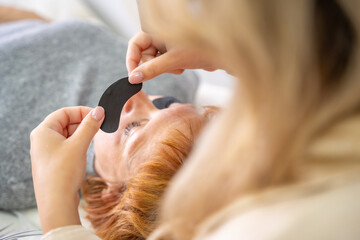 Naklejka premium Close-up of beautician hands holding black under-eye patch before UV eyelash extension. Professional tools preparation for modern lash enhancement technique.