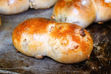 Close-up of a freshly baked walnut bread roll with a golden brown crust, resting on a rustic baking...