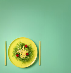 Pastel yellow plate of fresh green salad with cherry and grated cheese, on light green background. Fresh and healthy salad, slimming and modern food concept.