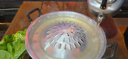 Pour the hot broth from the vintage kettle into the Pan roasted pork for the Thai barbecue Grill Pork. Barbecue buffet pig pan and vegetables in soup. Meat is often placed above the broth to cook.
