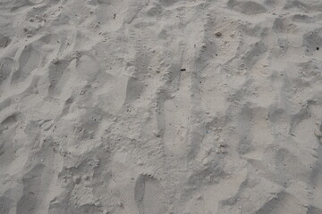 Textured sandy beach surface with unique patterns and footprints in soft white sand
