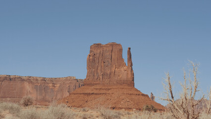 Fototapeta premium Shot in movement through dry hot desert with snags in monument valley in wild west of United States. Huge rock outcrop massifs of red and orange sandstone buttes destroyed by erosion.